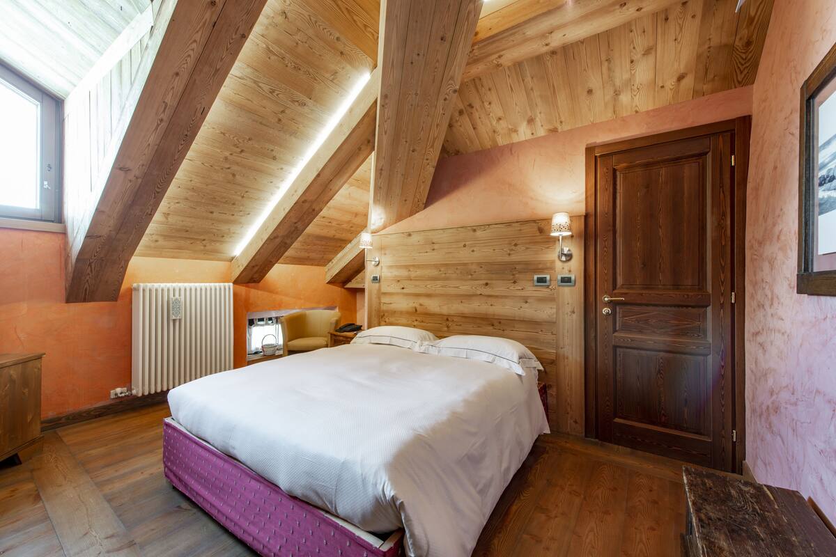 A wooden bedroom with a bed, a radiator, and a door.