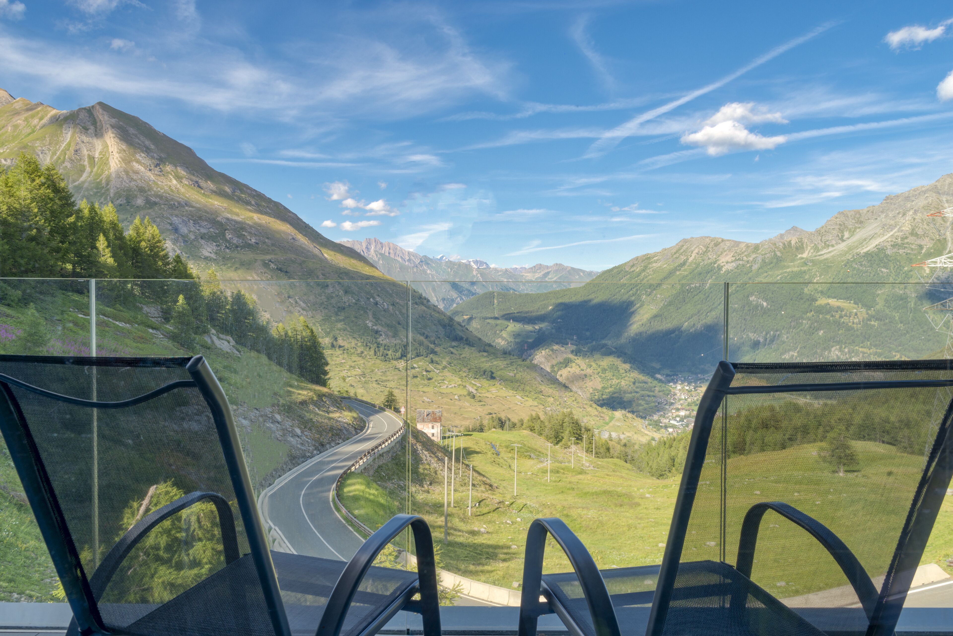 A scenic view from a high vantage point overlooking a winding road through a valley with mountains in the background.