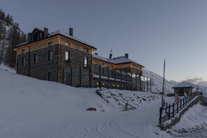 A snow-covered building with a restaurant, bar, and hotel signs, surrounded by a wooden fence and snow-covered ground. - Re delle Alpi (La Thuile)