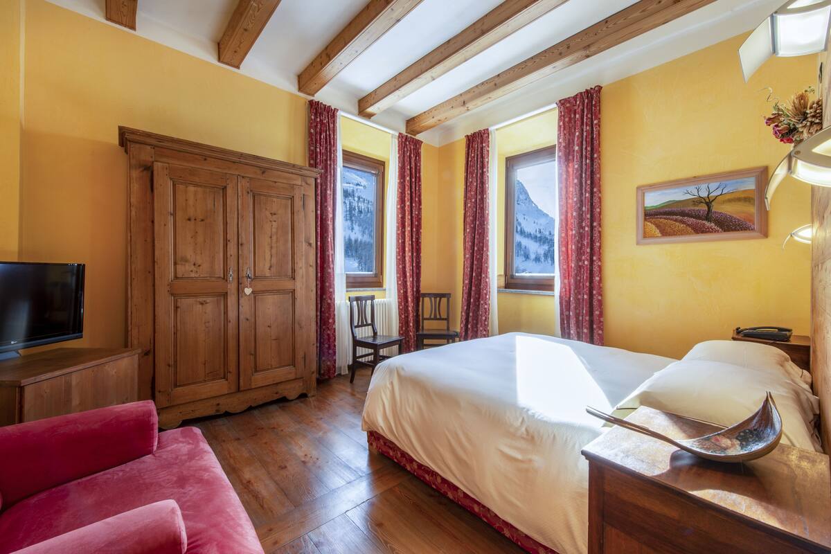 A bedroom with a bed, wooden wardrobe, a TV, and a red sofa.