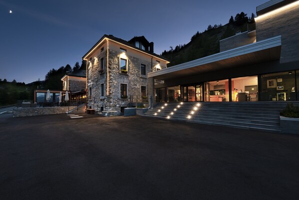 A modern house with a stone facade, a large glass entrance, and a well-lit driveway. - Re delle Alpi (La Thuile)