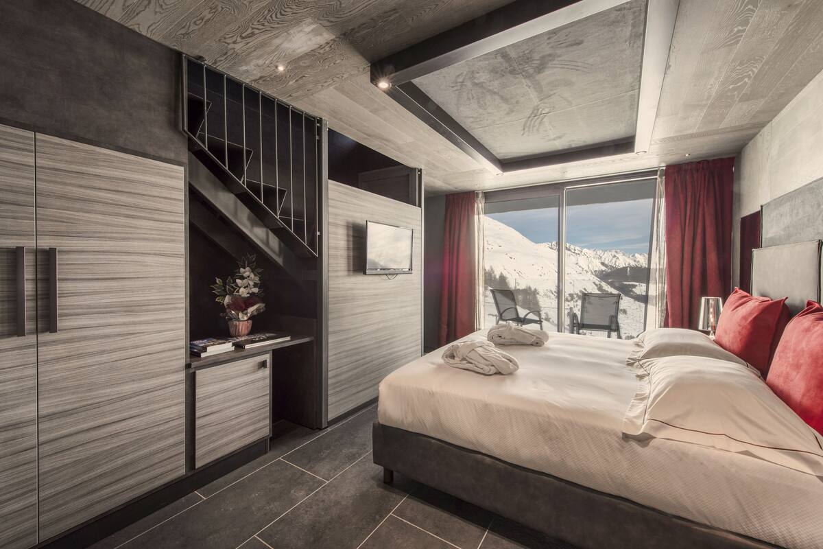 A modern bedroom with a large bed, a TV, a desk, and a staircase.