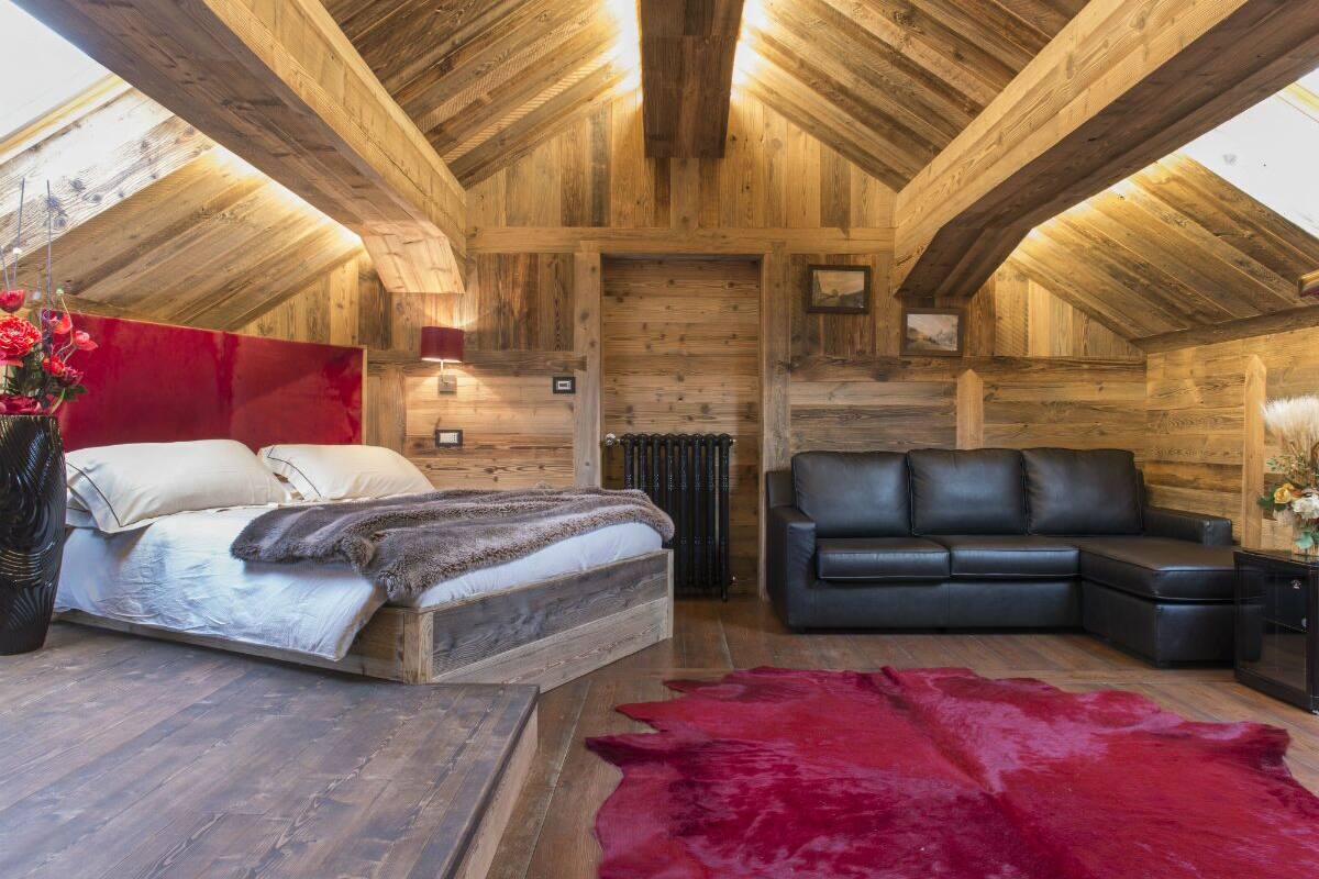 A log cabin interior with a wooden ceiling, a bed, a sofa, and a red rug.