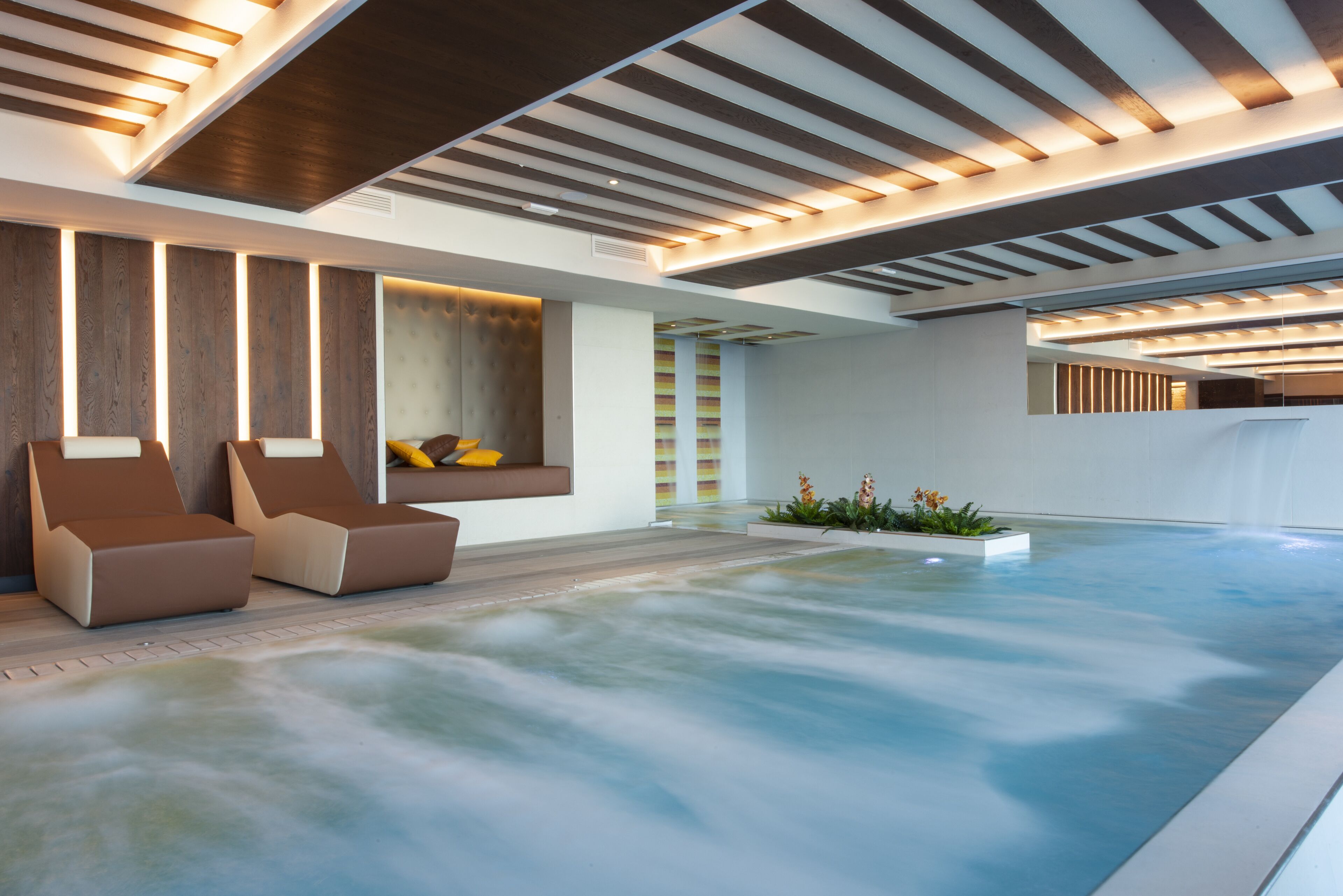 Een modern binnenzwembad met ligbedden en een sfeervolle wellness-omgeving.