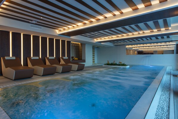 A modern indoor pool area with lounge chairs and a ceiling with linear lighting. - Re delle Alpi (La Thuile)