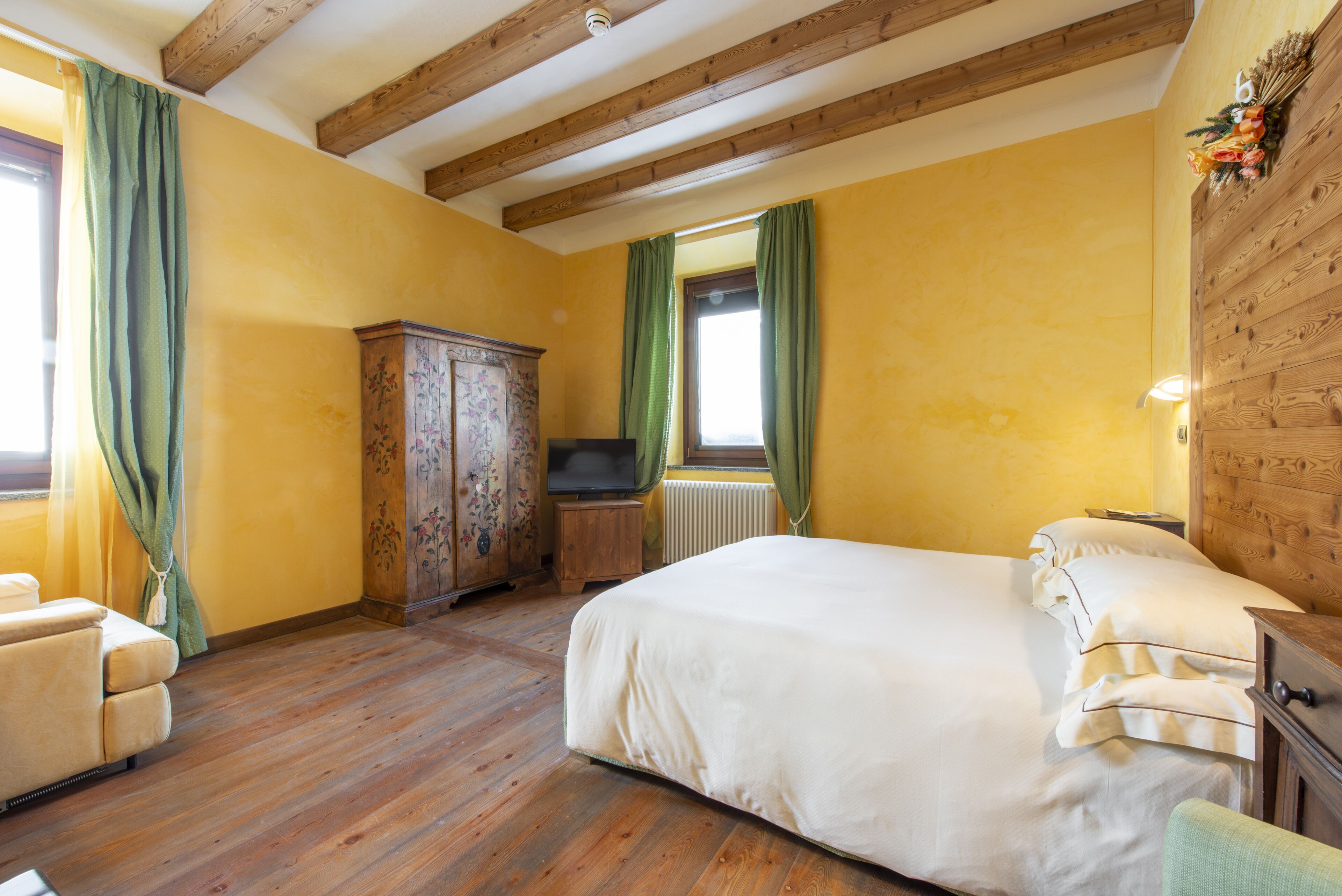Une chambre avec un plafond en bois, un lit recouvert de draps blancs, une armoire en bois et un téléviseur.