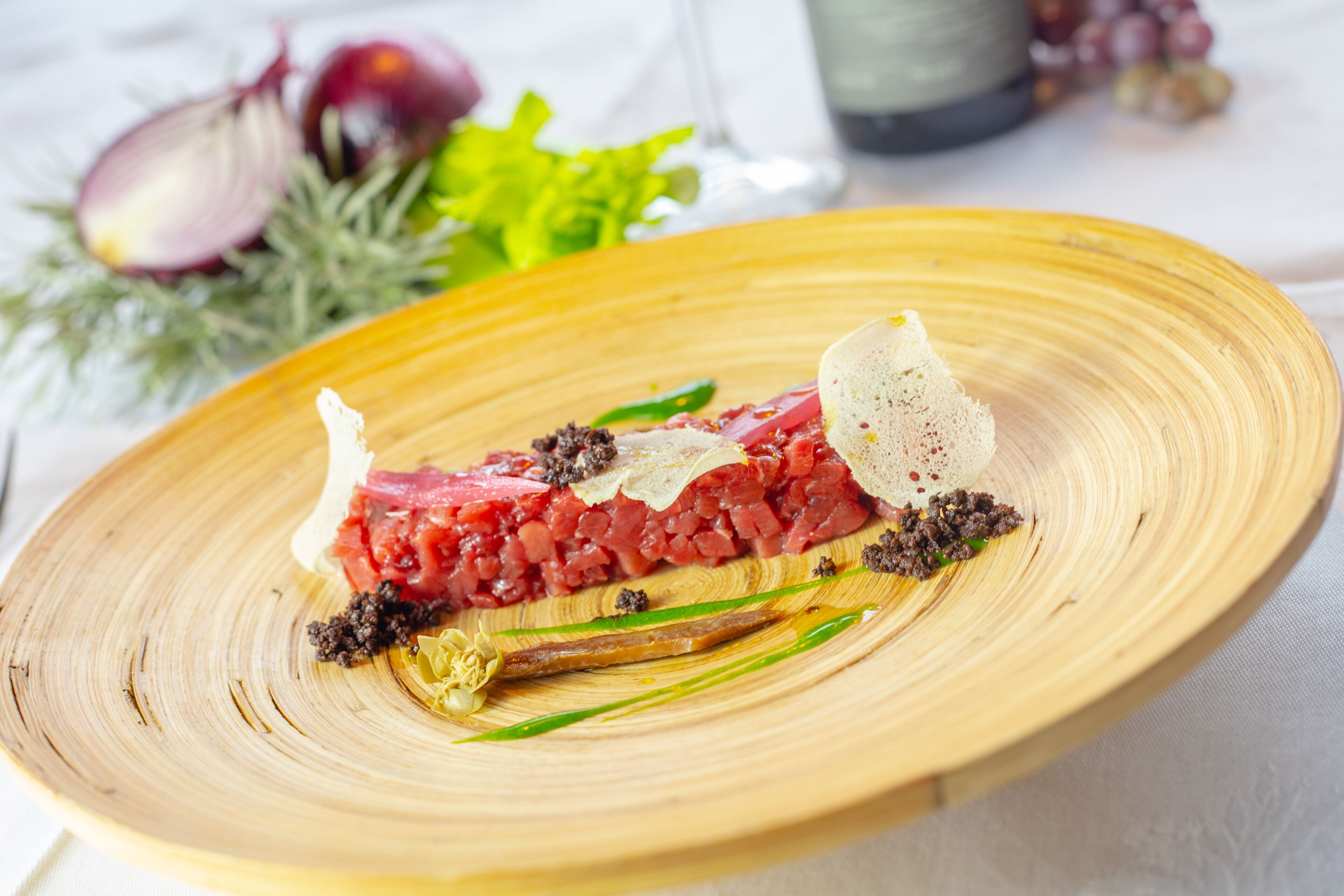 Une assiette en bois contenant un plat de viande crue, agrémenté d’herbes et d’épices.