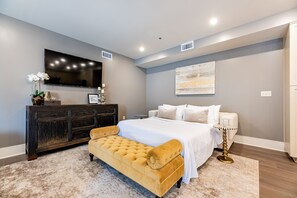 A bedroom with a bed, a chest of drawers, a bench, a TV, and a painting on the wall.