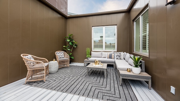 Een moderne patio met een bank, twee rieten stoelen, een bijzettafeltje en een bloempot.