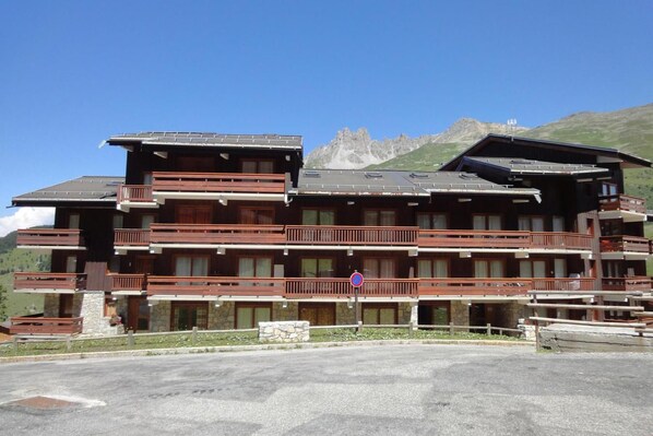 A multi-story hotel with balconies, a stone facade, and a mountainous backdrop.