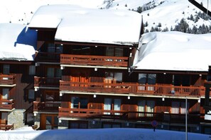 A multi-story wooden building with balconies, surrounded by snow-covered terrain and trees.