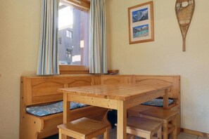 A wooden dining area with benches and a table, a window with curtains, and a wall-mounted picture.