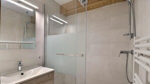 Een moderne badkamer met een glazen douchecabine, een wastafel met spiegel en een handdoekrek.