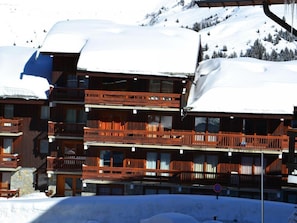 A multi-story wooden building with balconies, surrounded by snow-covered mountains.