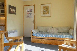 A room with a bed, a wooden bench, a radiator, a door, and a poster on the wall.