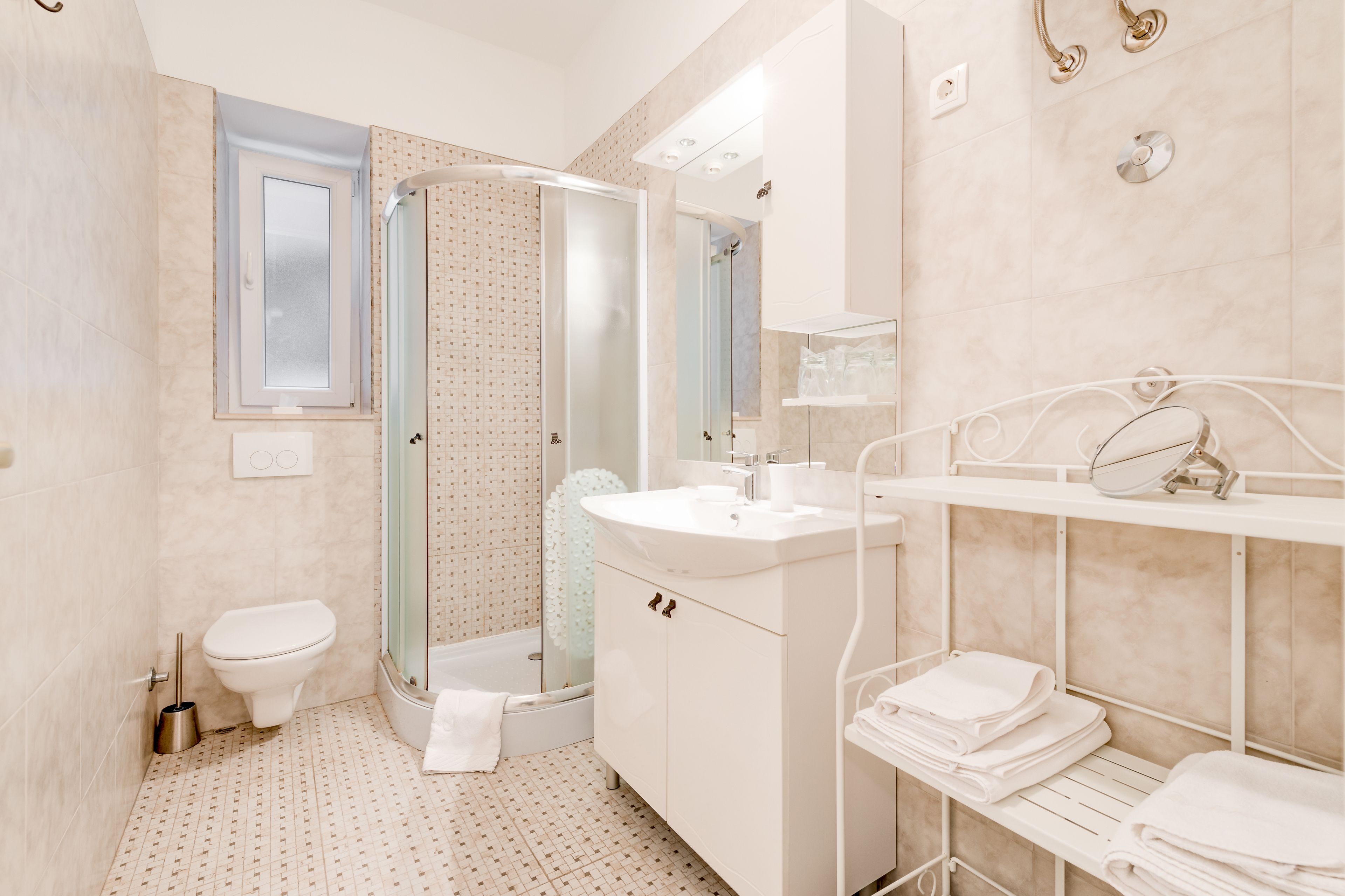 Un bany modern amb dutxa de vidre, un vàter, un lavabo amb mirall i un penjallatoiles.