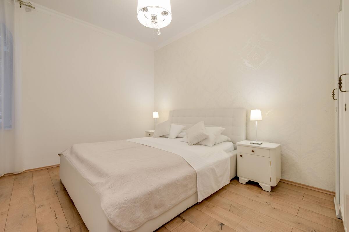 Une chambre à coucher avec un grand lit, deux tables de chevet avec des lampes et un lustre.