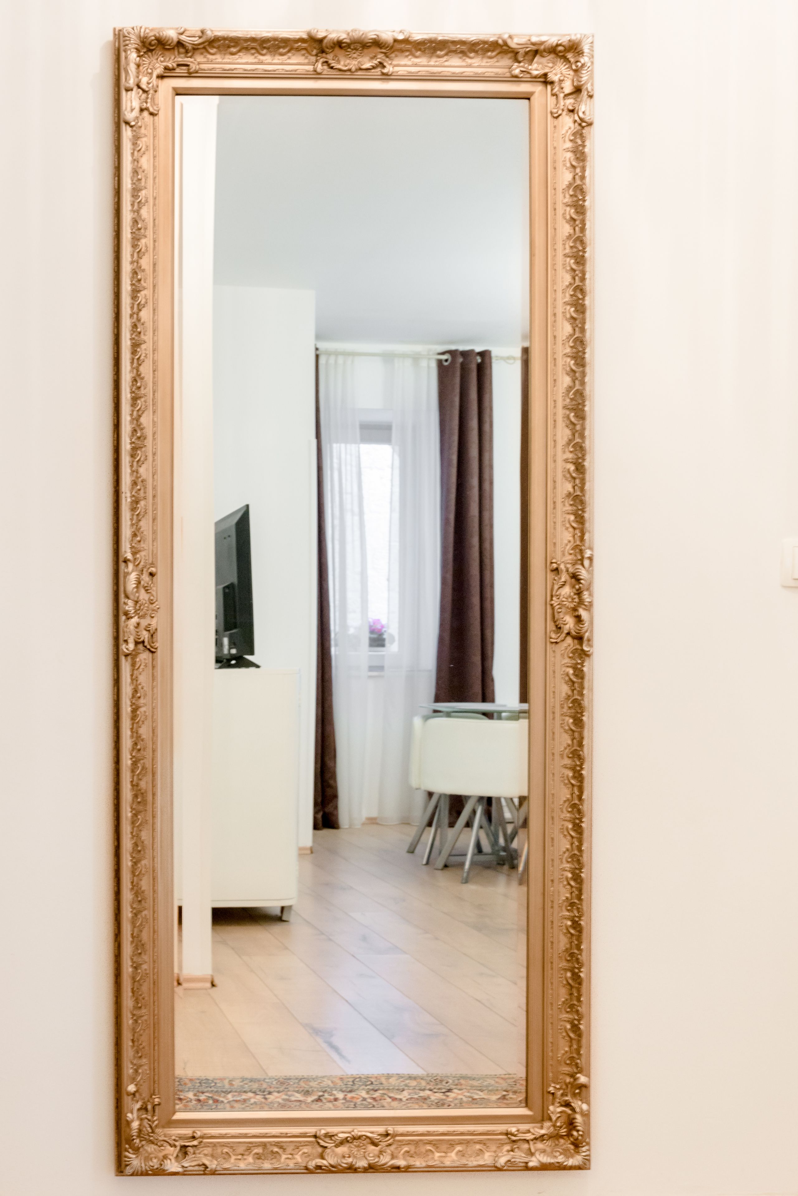 A room with a large ornate mirror, a television, and a desk with a chair.