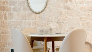 A dining area with a stone wall, a round mirror, and four chairs with wooden legs. - Aurum Templi Suites (Split)