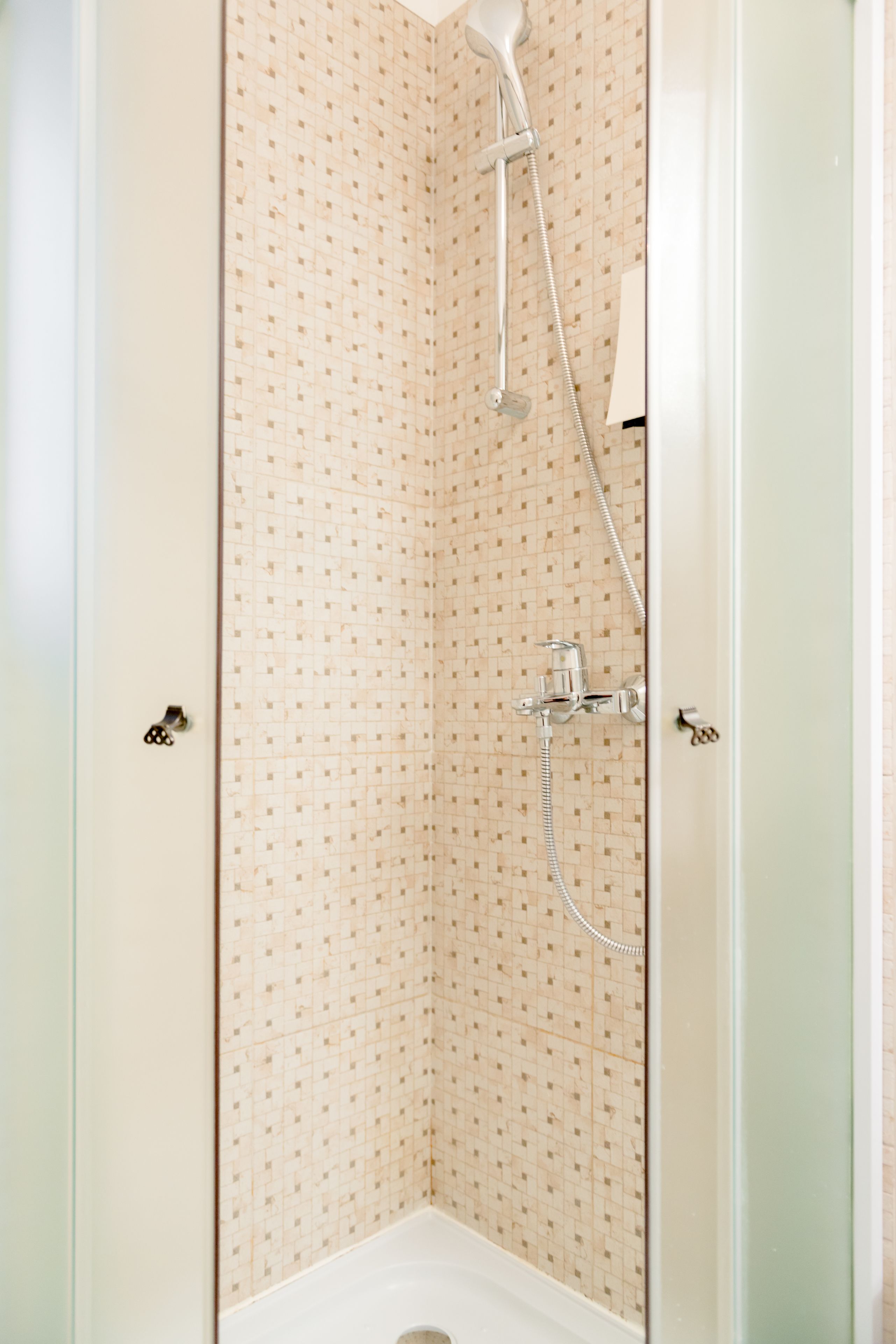 A small, enclosed shower area with a tiled wall and a handheld showerhead.