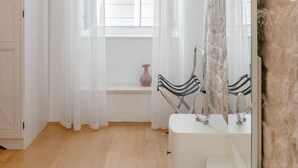 A bathroom with a white vanity, a mirror, a window with sheer curtains, and a rustic stone wall. - Aurum Templi Suites (Split)