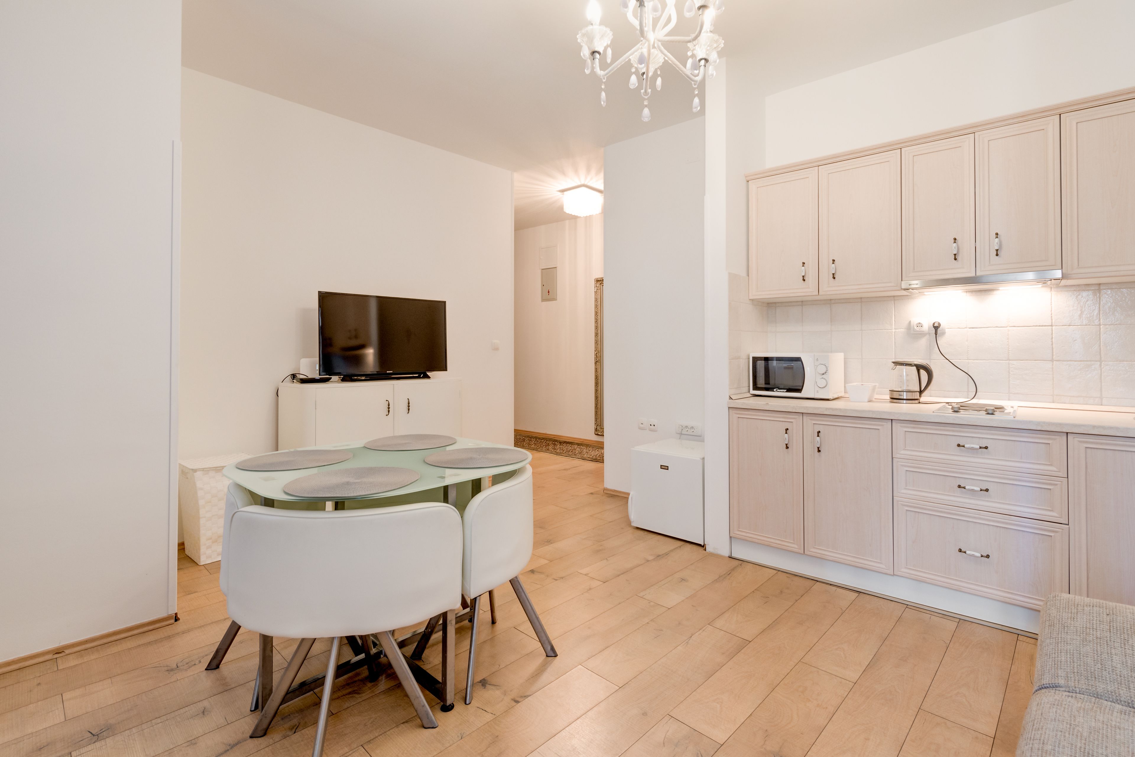 A modern kitchen with white cabinets, a microwave, and a glass-top dining table with chairs.