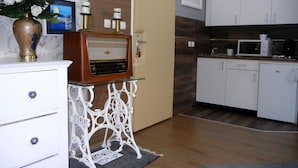 Een compacte keuken met witte kastjes, een vintage radio op een decoratieve standaard, en een magnetron op het aanrecht.