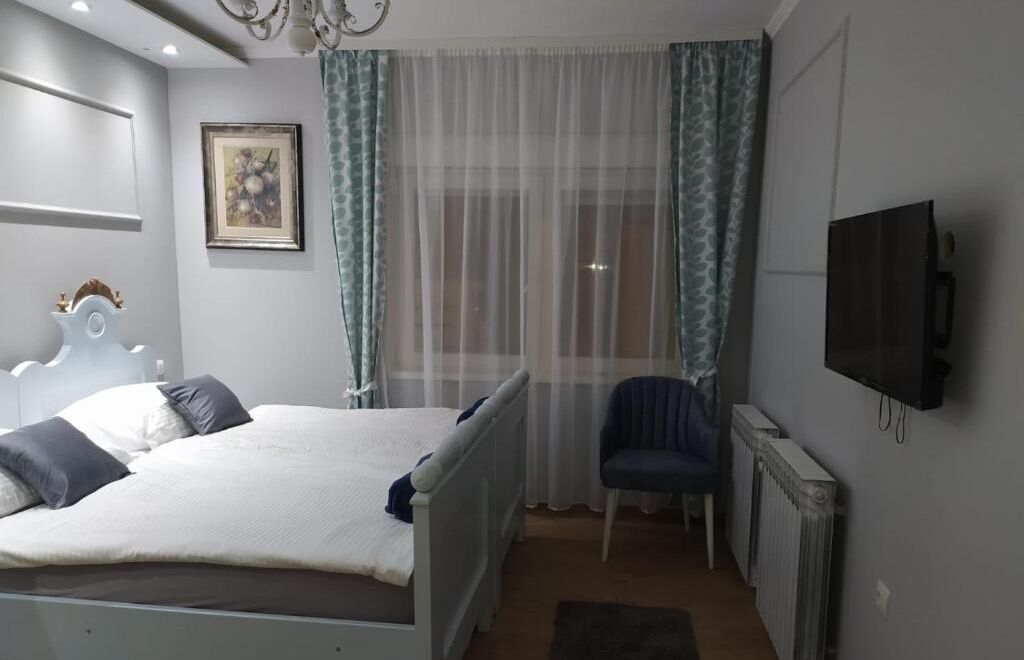 A bedroom with a bed, a chair, a TV, and a radiator.