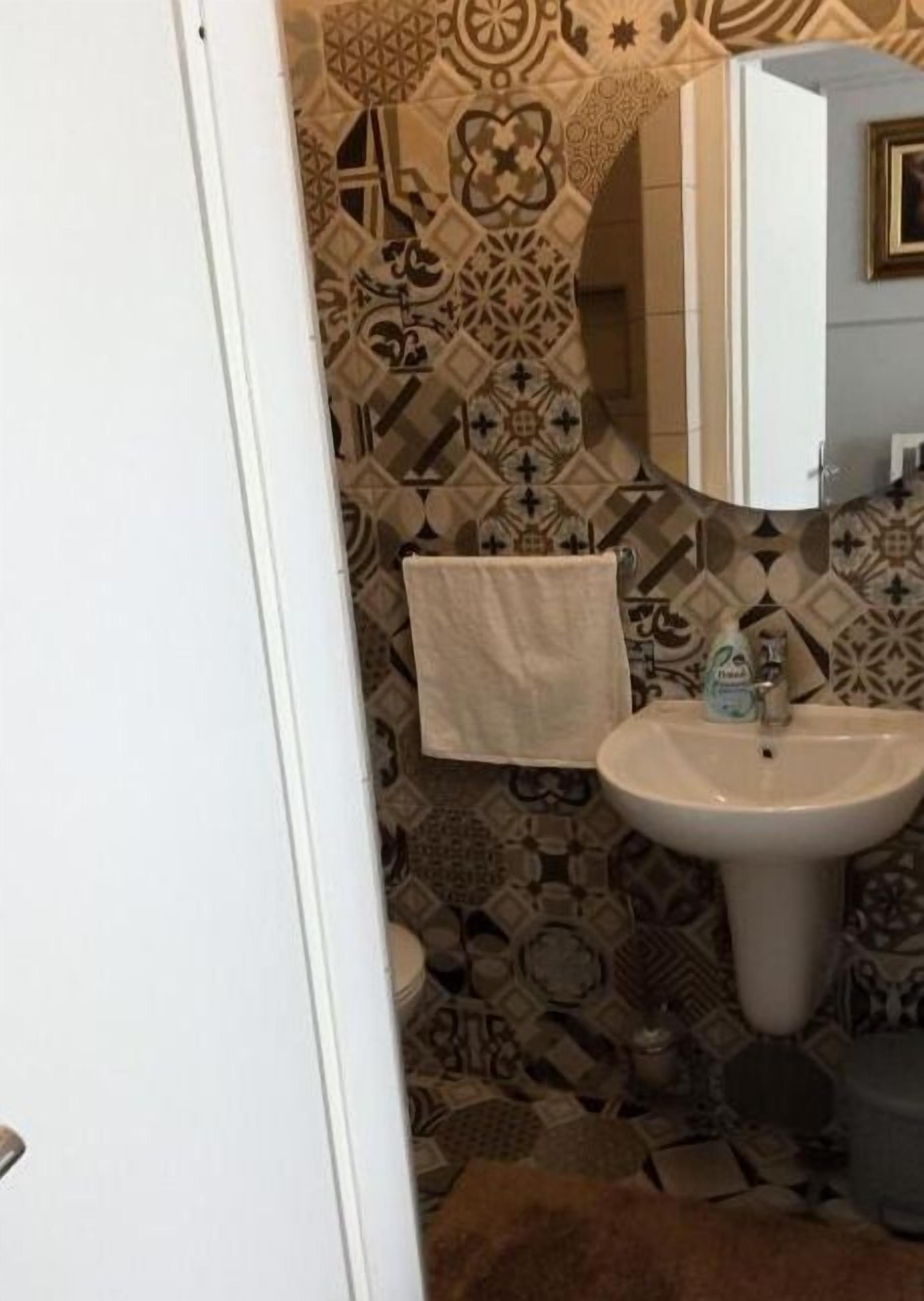 Ein Badezimmer mit gemusterten Fliesen, einem Waschbecken und einem Handtuch an der Wand.
