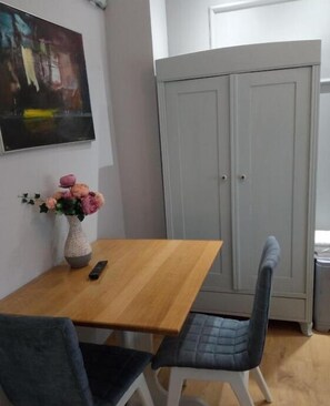 A small dining area with a wooden table, two chairs, a vase with flowers, and a painting on the wall. - Villa Lucia Apartments & Rooms (Slavonski Brod)
