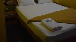 Een hotelkamer met een bed, een nachtkastje, een wandlamp en een kamerplant.