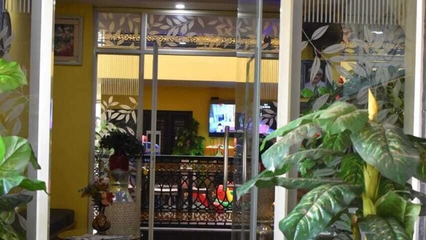 Een hotelingang met een glazen deur, binnenshuis planten en een zichtbaar interieur met een televisie en meubels.