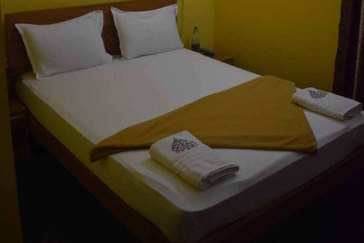 Une chambre d’hôtel avec un lit, des oreillers blancs, une couverture jaune et une petite table de chevet avec une lampe.