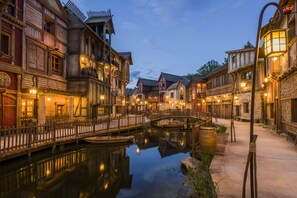 A historic European-style street with wooden buildings, a canal, and a bridge. - Les Quais de Lutèce (Plailly)