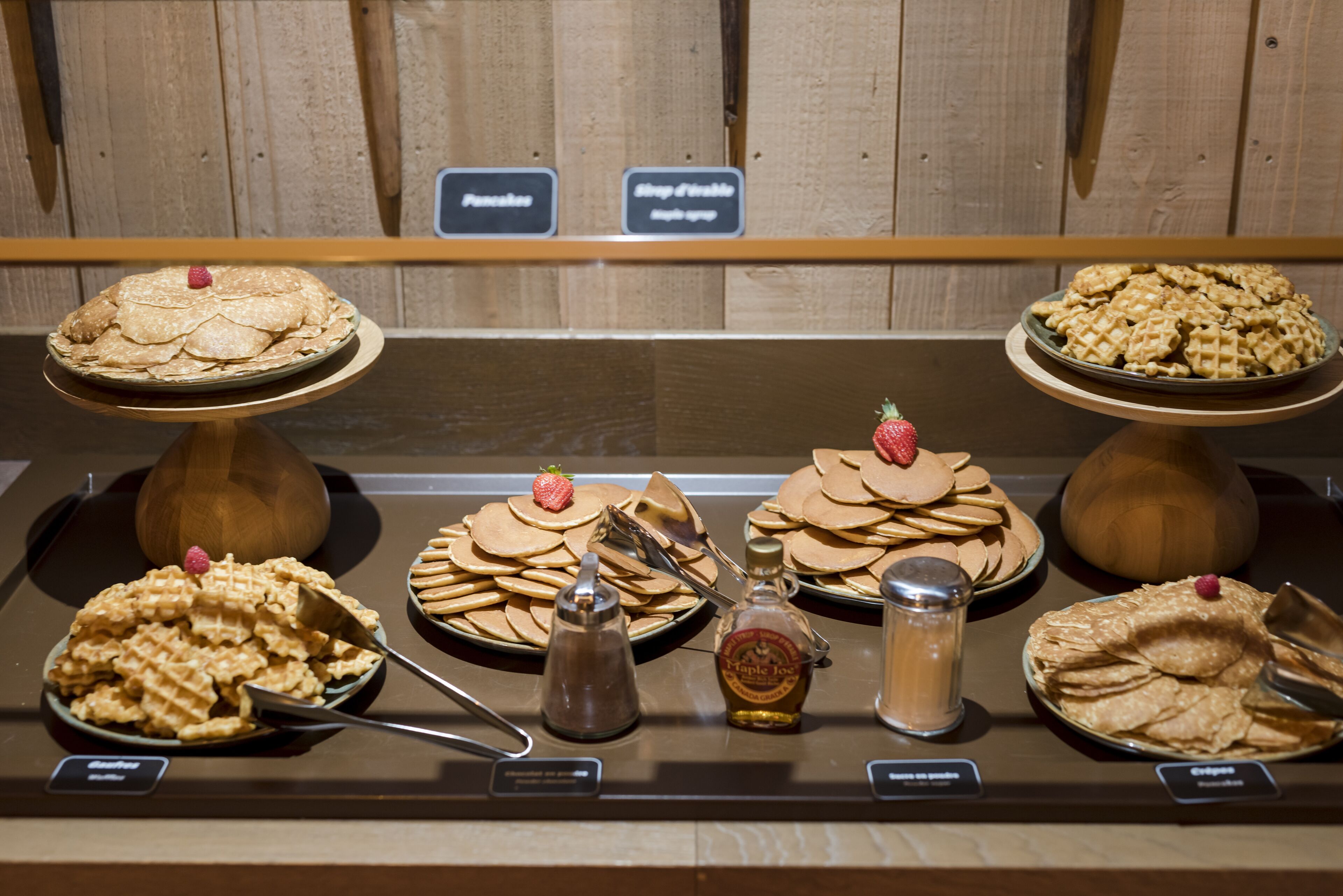 A dessert display with various types of pancakes and waffles, each garnished with a strawberry.