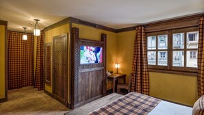 A hotel room with a bed, a television, a desk with a chair, a lamp, and a window with curtains. - Les Quais de Lutèce (Plailly)