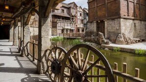 A rustic wooden building with stone walls and a wooden bridge over a pond. - Les Quais de Lutèce (Plailly)