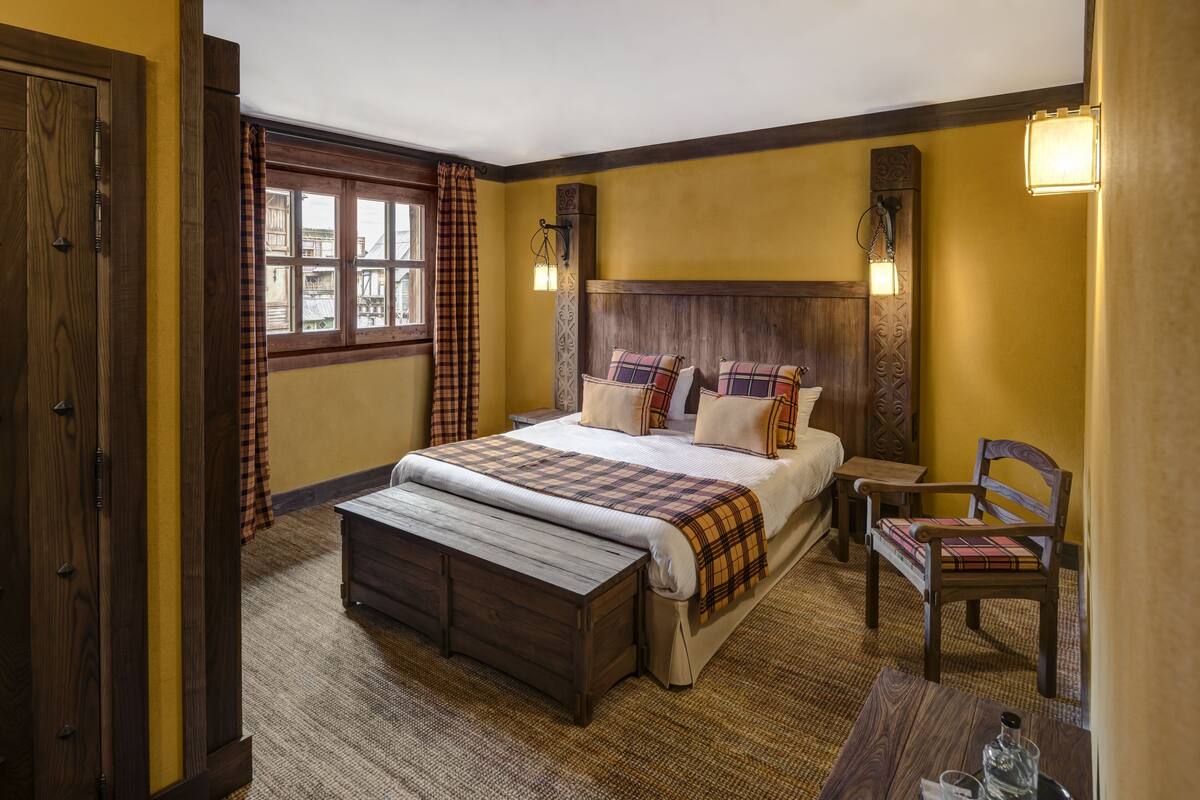 Quarto com uma cama grande, um banco de madeira, uma cadeira e uma mesa de cabeceira.