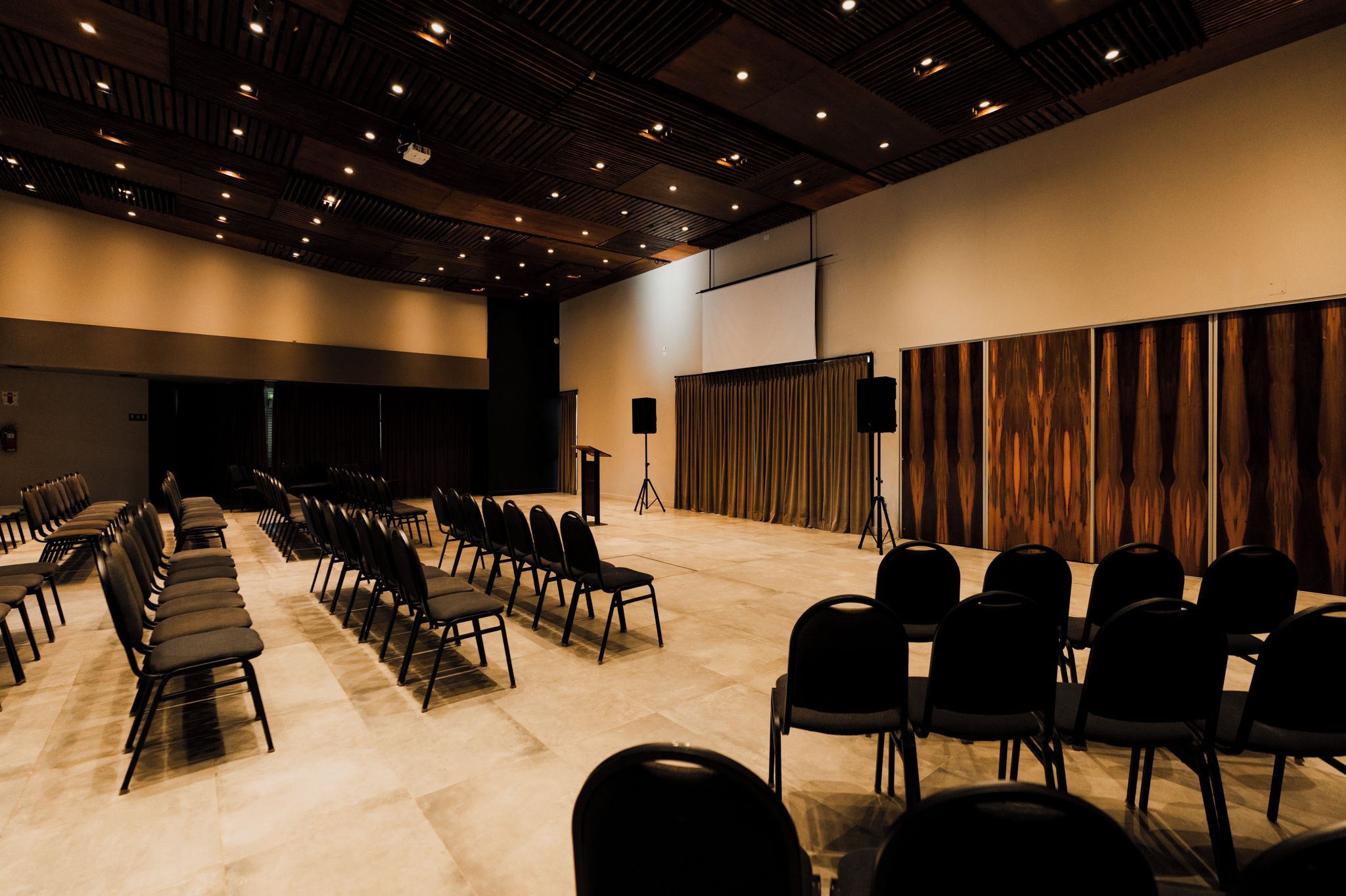 A conference room with rows of chairs, a podium, a projector screen, and a sound system.