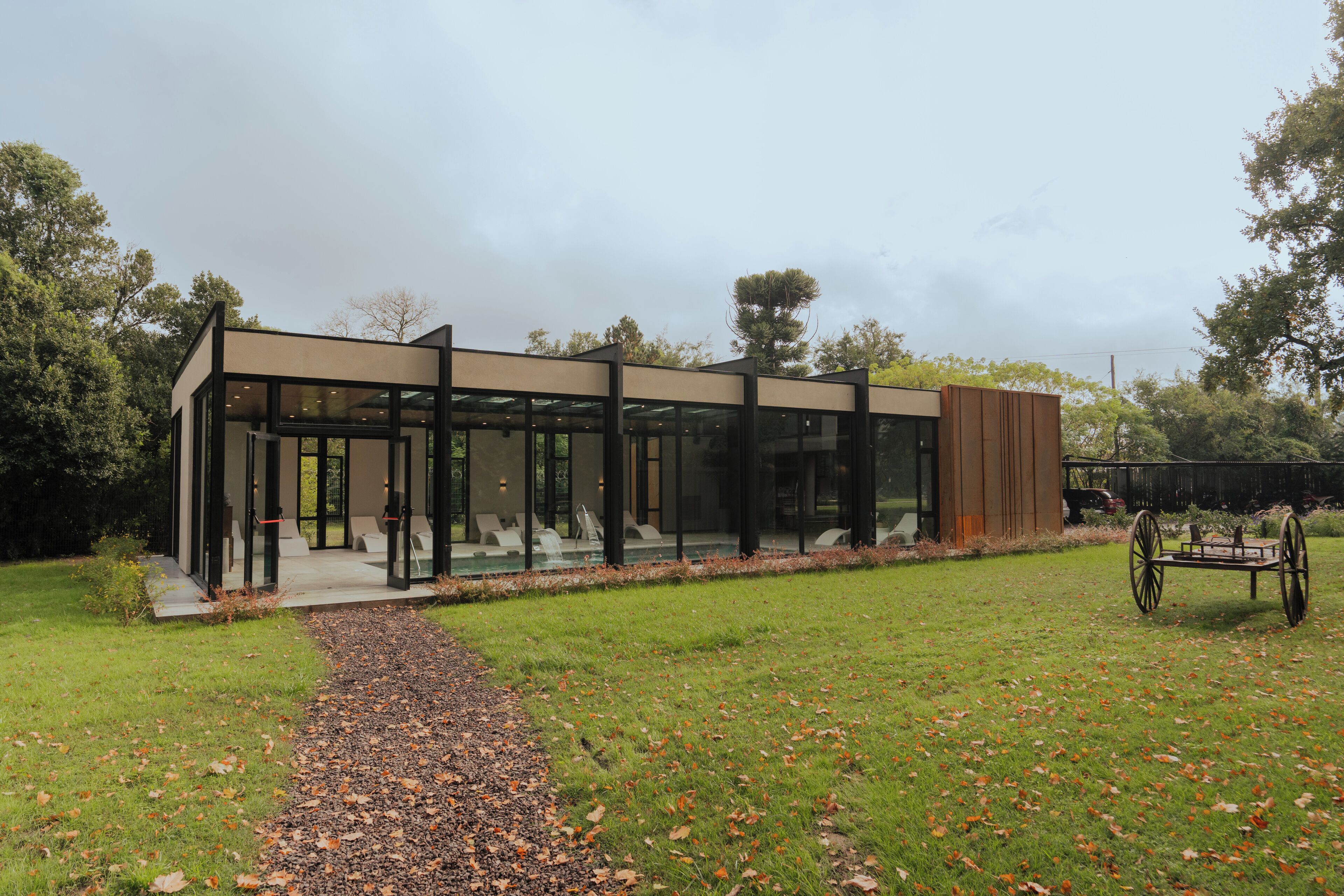 A modern building with large glass windows, a gravel path leading to it, and a carriage in the foreground.