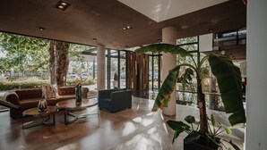 Un vestíbulo amplio con diseño moderno, que incluye una planta en maceta grande, sofás de cuero y una mesa de centro.