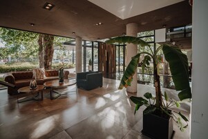 Un vestíbulo amplio con diseño moderno, que incluye una planta en maceta grande, sofás de cuero y una mesa de centro.