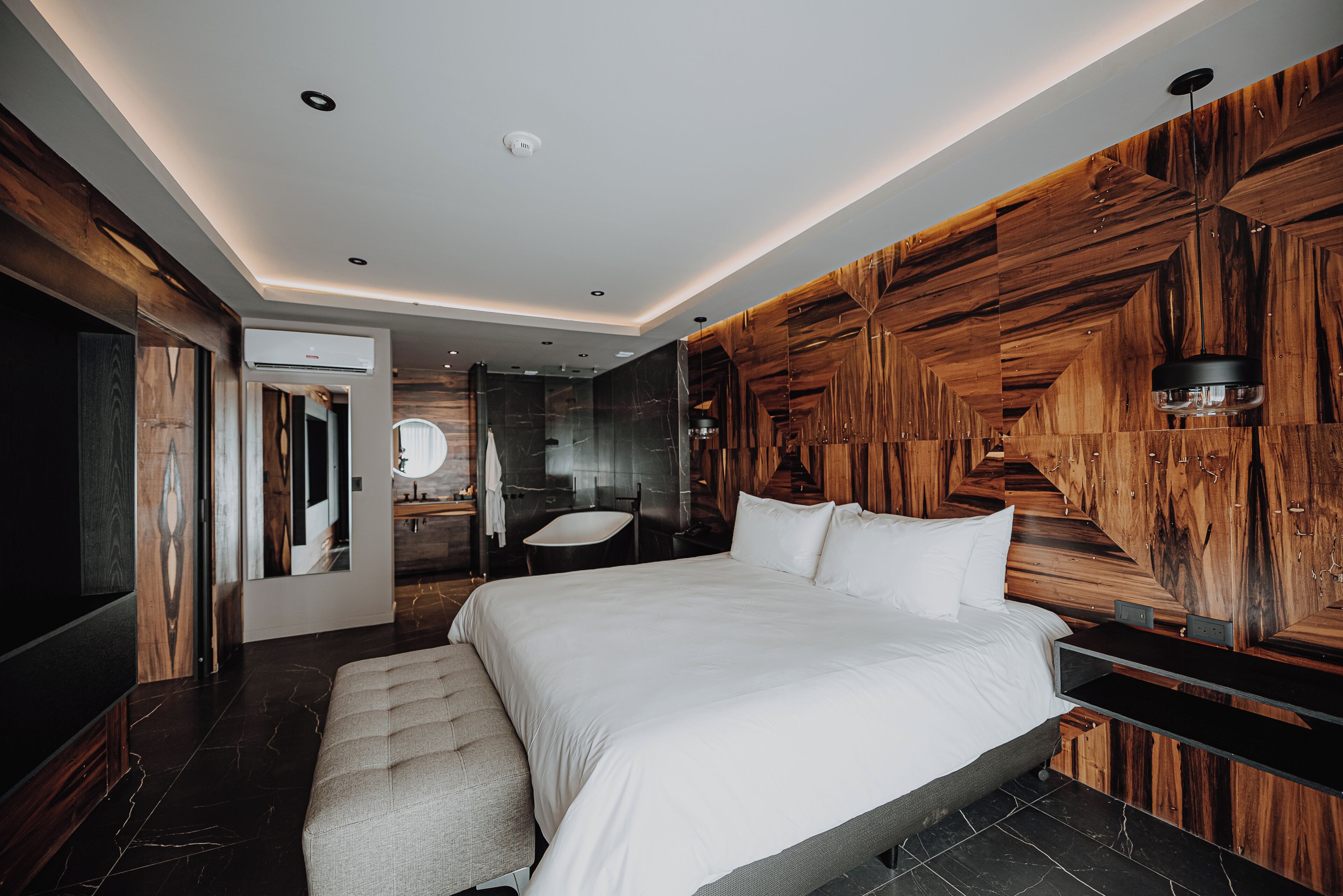 A modern bedroom with a large bed, a wooden accent wall, and a built-in bench.