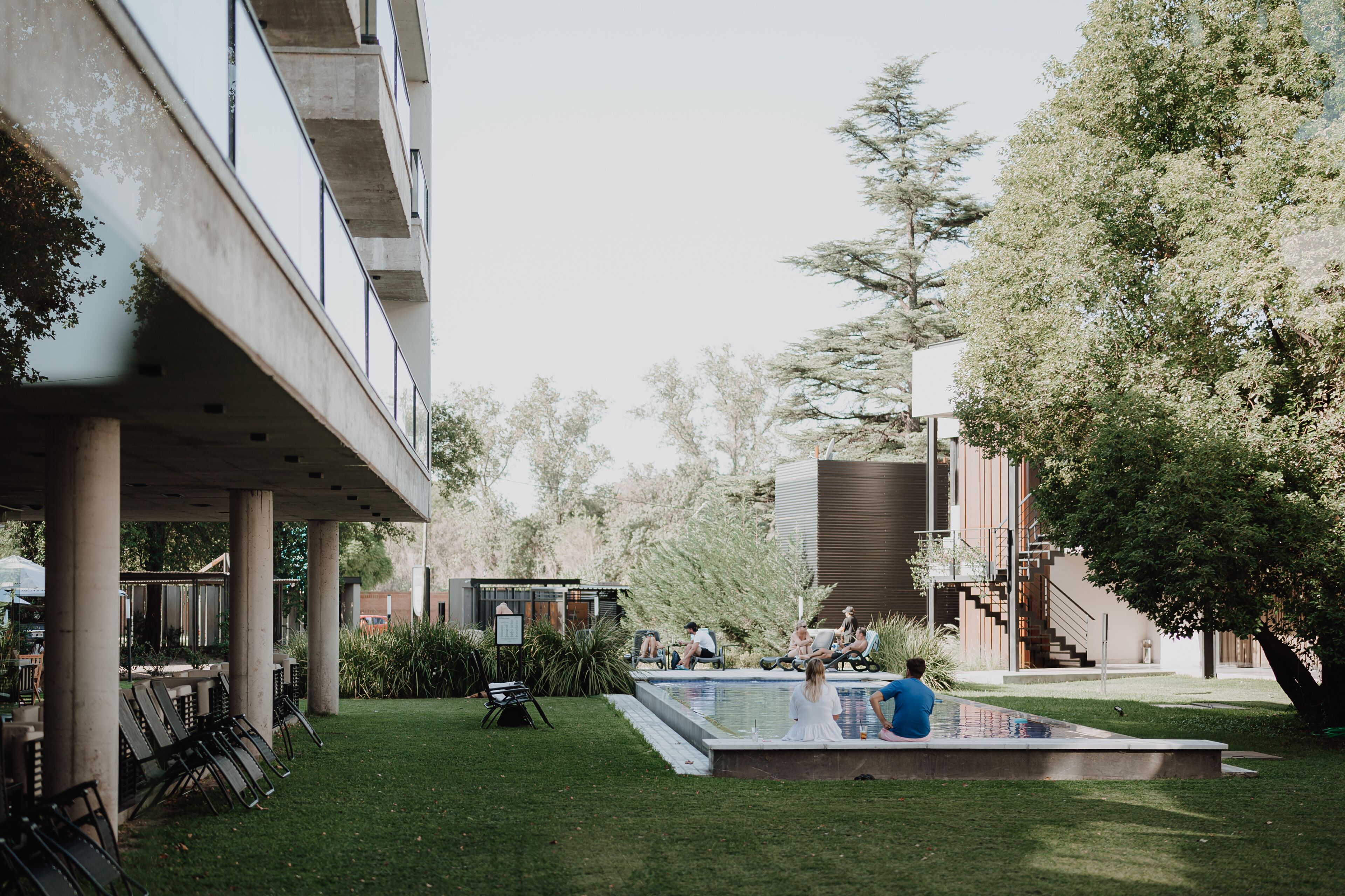 Un patio con piscina, zonas de estar y un edificio moderno con escalera.