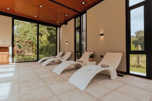 Un salón moderno y luminoso con grandes ventanales, sillones blancos y techo de madera.