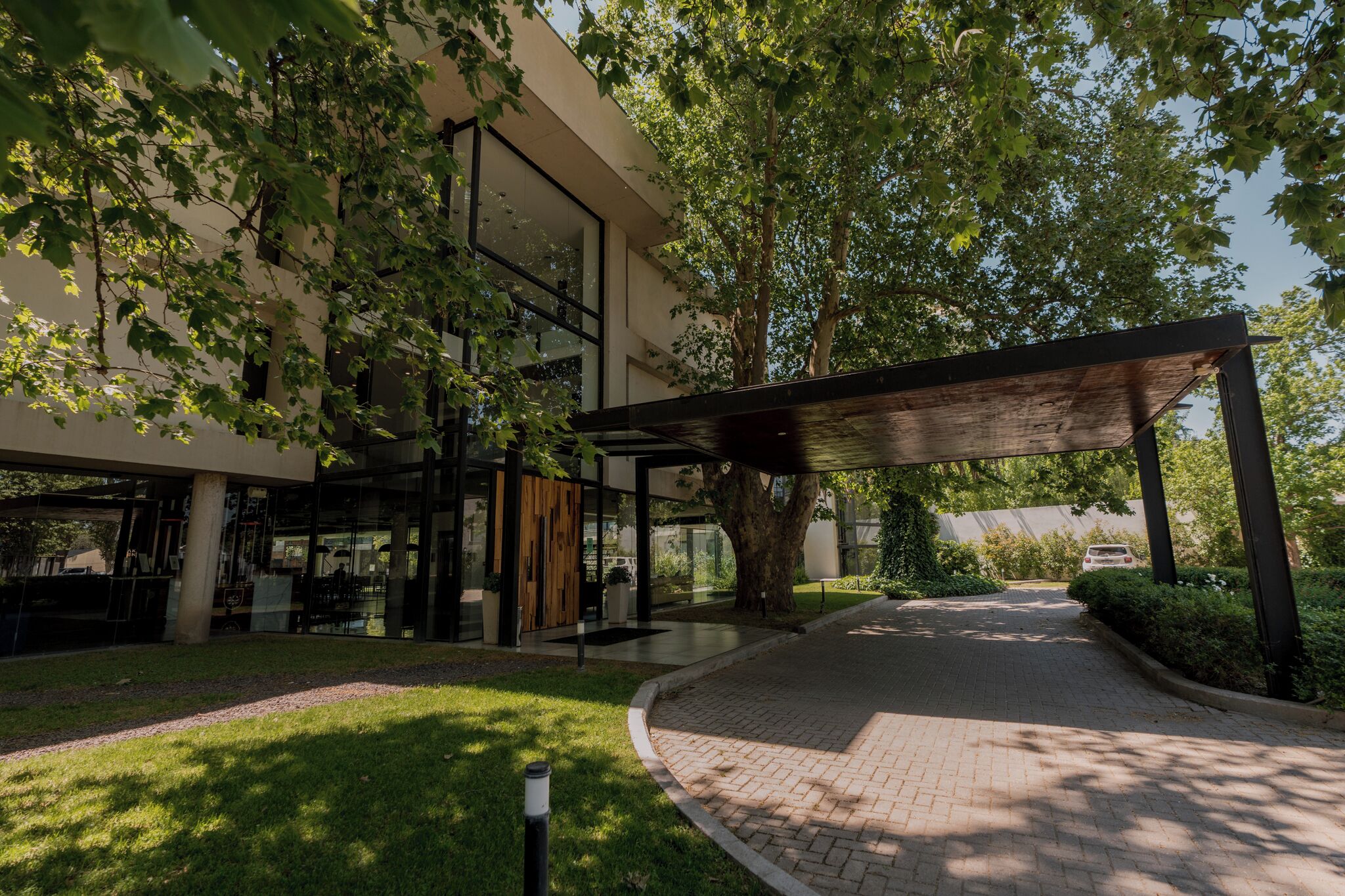 A modern building with a glass facade, a covered outdoor seating area, and a paved pathway.