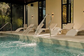 A swimming pool with a water feature, surrounded by lounge chairs and a modern building facade. - La Urumpta Hotel, AKEN MIND (Rio Cuarto)
