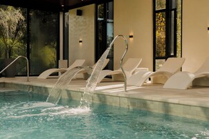 Una piscina con fuente, rodeada de sillas de descanso y una fachada de edificio moderna.