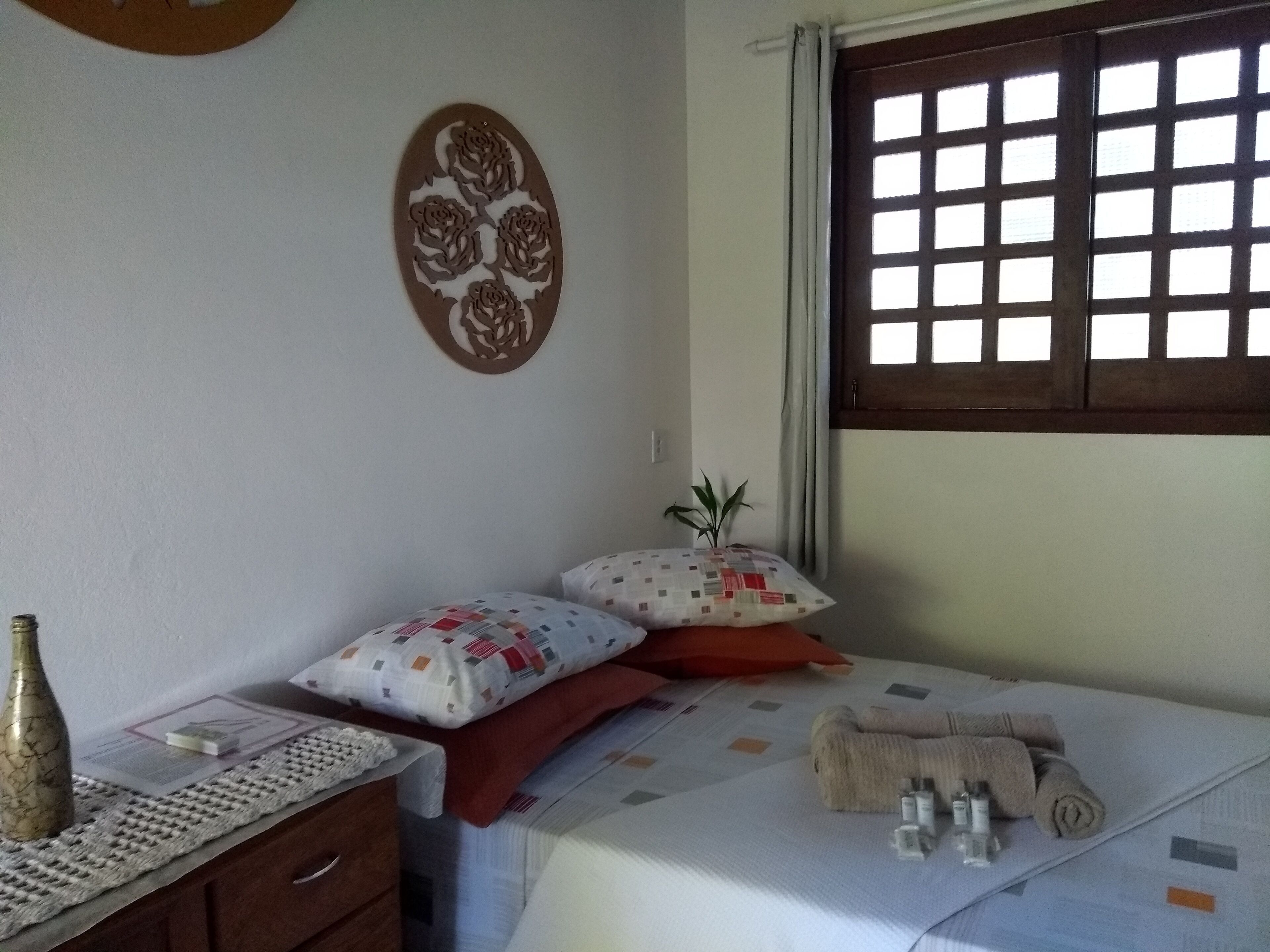Une chambre à coucher avec un lit, des oreillers, une table de chevet avec une bouteille, un élément de décoration murale et une fenêtre à motifs géométriques.