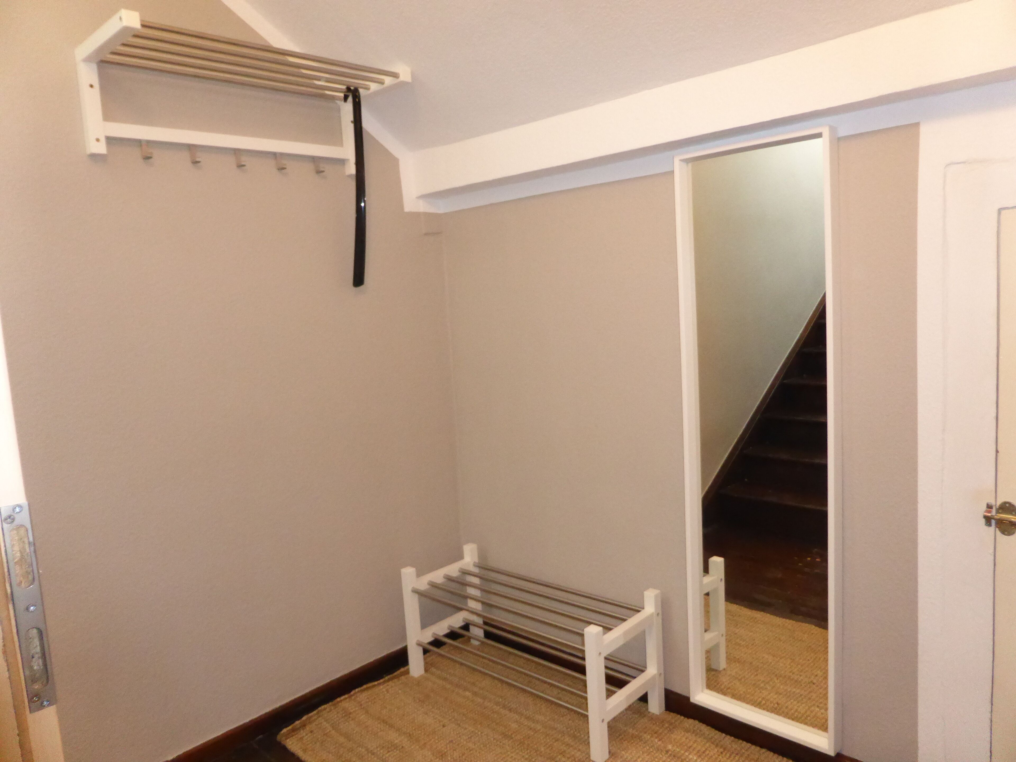 A narrow hallway with a white door, a mirror, and a metal rack on the wall.